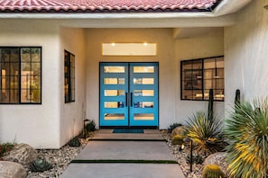 A house with a blue door, a small garden with rocks and cacti, and a tiled roof. - The Donna House - A Ryson Property (Palm Springs)