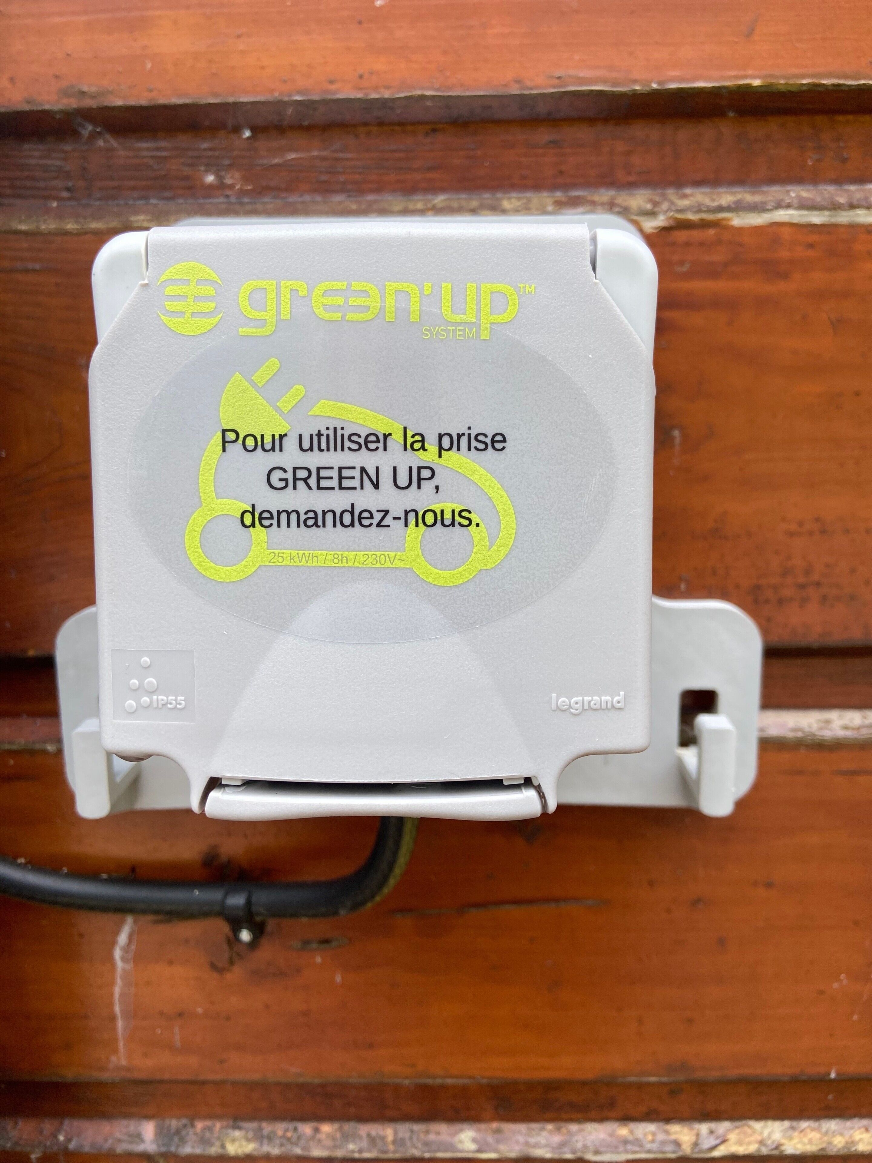 A grey electrical box with the text 'green up' and 'Pour utiliser la prise GREEN UP, demandez-nous.'