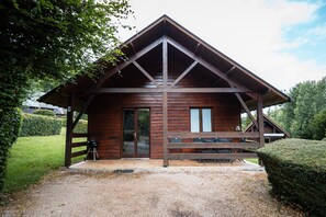 Une cabane en bois avec un porche, un barbecue et une allée gravillonnée.