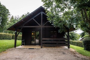Une cabane en bois avec un porche couvert, un barbecue à l’extérieur et une pelouse bien entretenue.
