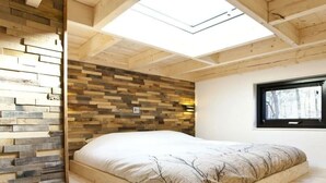Een kamer met een bed, houten wandpanelen, een dakraam en een raam.
