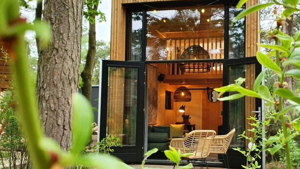 Een moderne houten hut met glazen deuren, een zithoek met rieten stoelen, en een hanglamp.