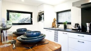 Een moderne keuken met witte kasten, zwarte aanrechtbladen en een houten eettafel.
