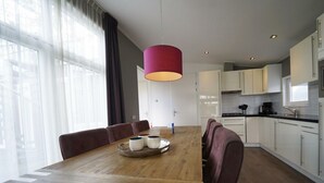 Ett modernt kök med vita skåp, ett matbord i trä och en röd hänglampa.