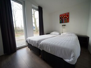 Ein Hotelzimmer mit einem großen Bett, einem Nachttisch, Vorhängen an einem Fenster und einem an der Wand hängenden Kunstwerk.