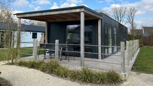 Ein modernes Haus mit überdachter Terrasse, großen Fenstern und einer Holzterrasse.