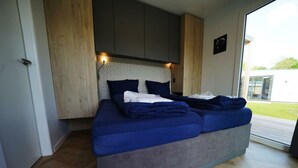 Ein modernes Schlafzimmer mit einem großen Bett, Holzvertäfelung und Blick ins Freie.