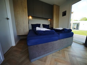 A modern bedroom with a large bed, wooden paneling, and a view of the outdoors. - Holiday Home in Kaatsheuvel With Terrace (Kaatsheuvel)