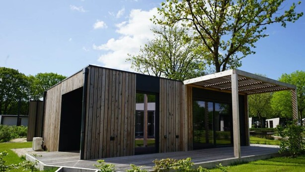 Ein modernes Gebäude mit Holzfassade, einer überdachten Außenfläche und einer grünen Landschaft.