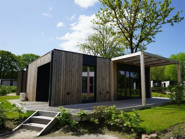A modern building with a wooden facade, a covered outdoor area, and a grassy landscape. - Holiday Home in Kaatsheuvel With Terrace (Kaatsheuvel)