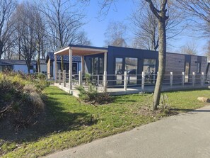 A modern building with a covered outdoor seating area, large windows, and a paved pathway. - Holiday Home in Kaatsheuvel With Terrace (Kaatsheuvel)