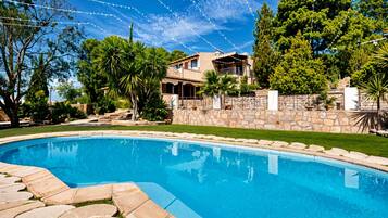Una piscina con escalones de piedra que la conducen, rodeada de un muro de piedra y vegetación.
