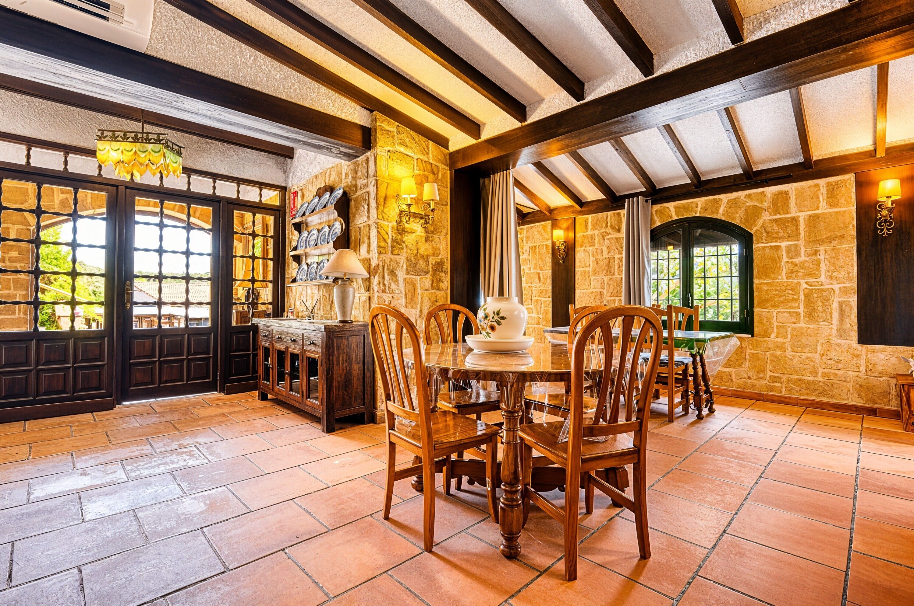A dining area with a stone wall, wooden ceiling beams, and a table set for four.