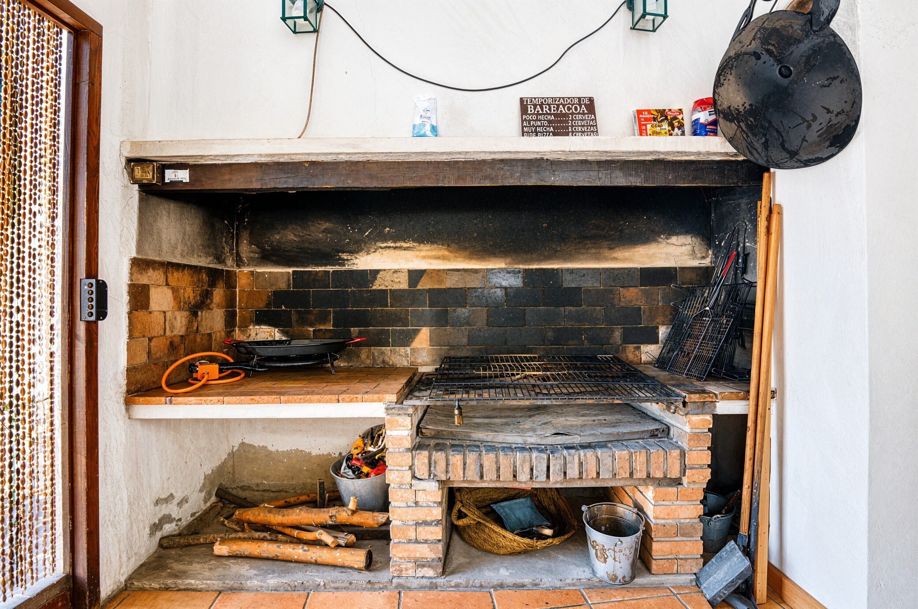 A brick oven with a metal rack, a hanging pot, and a sign above it.