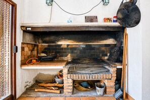 A brick oven with a metal rack, a hanging pot, and a sign above it.