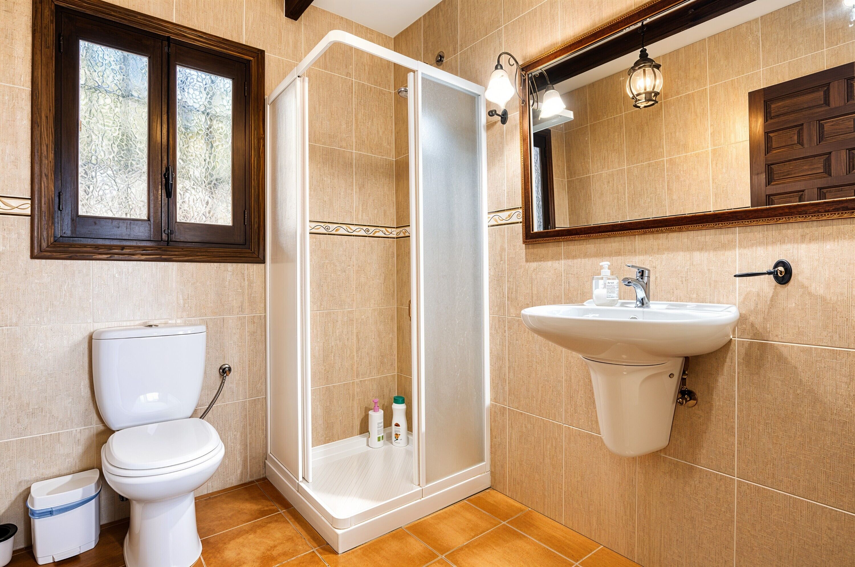 Une salle de bain comprenant des toilettes, une douche, un lavabo et une fenêtre avec un cadre en bois.