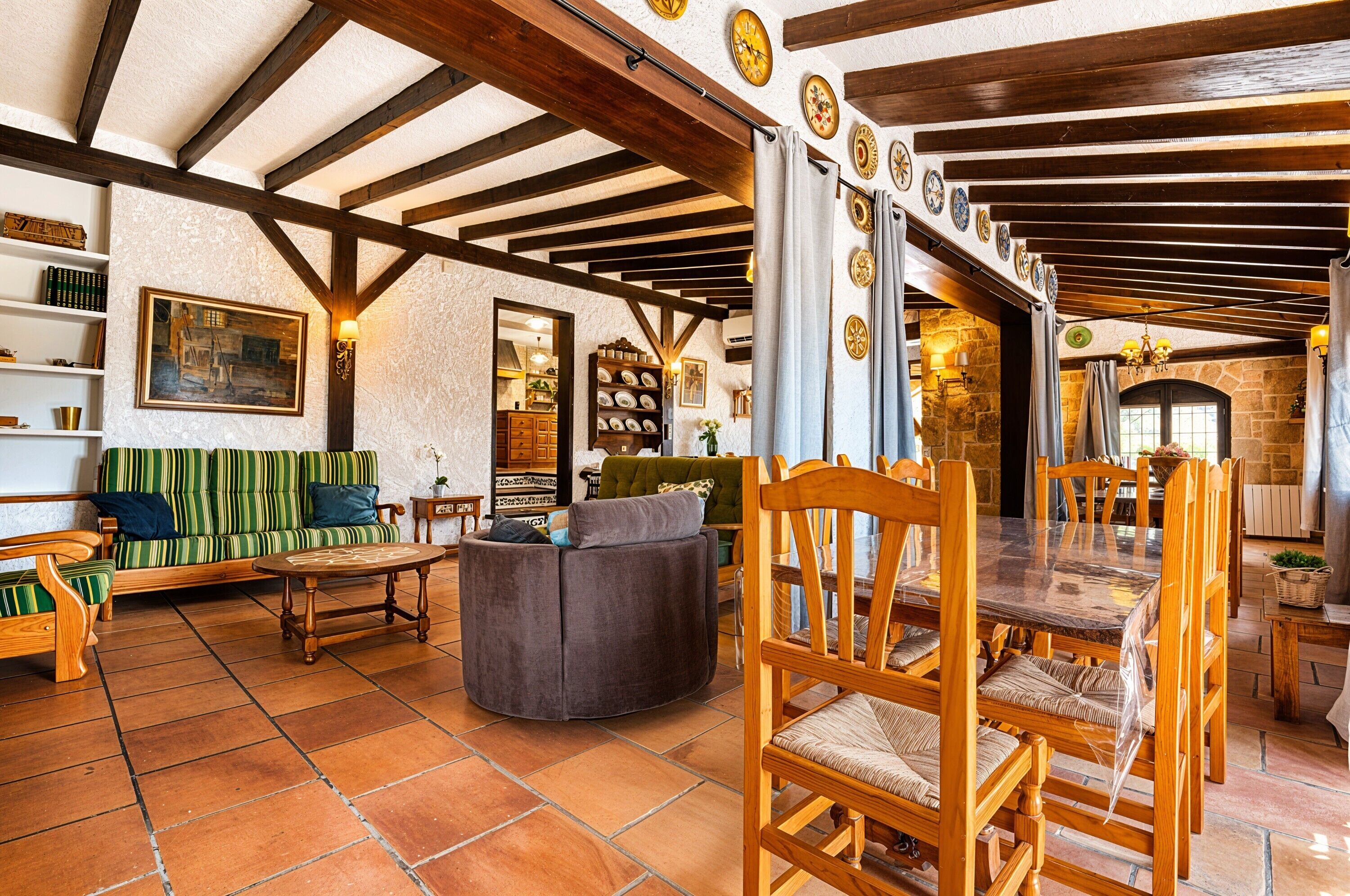 Un interior rústico con vigas de madera a la vista, un comedor con sillas y una mesa de madera, un sofá con cojines y una estantería.