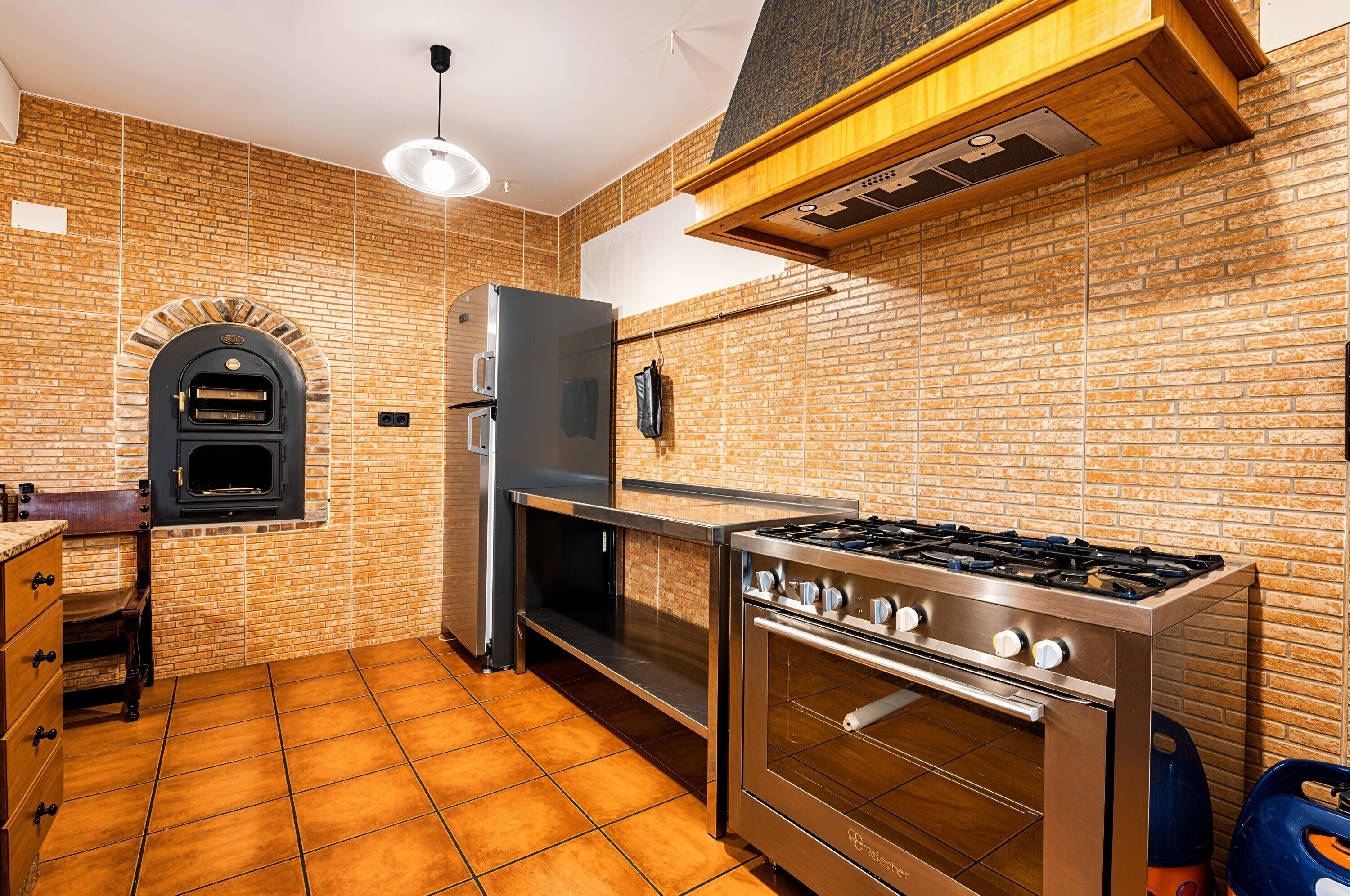 Une cuisine avec un mur en briques, un four encastré, une cuisinière à gaz et un réfrigérateur.