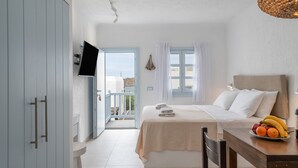 Et soveværelse med seng, et spisebord med frugt, et fjernsyn og en balkon.