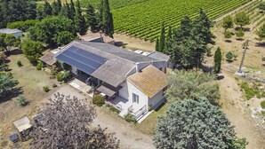 A large building with a sloped roof, surrounded by a vineyard, and a small detached structure with solar panels.
