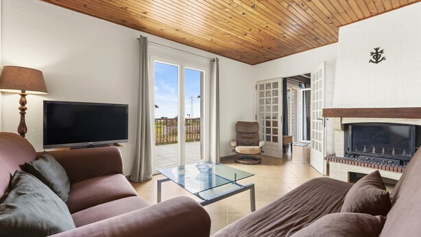 A living room with a TV, sofa, glass coffee table, fireplace, and sliding glass doors to a balcony.