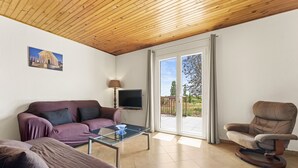 A living room with a sofa, a chair, a glass coffee table, a TV, and a sliding glass door leading to an outdoor area.