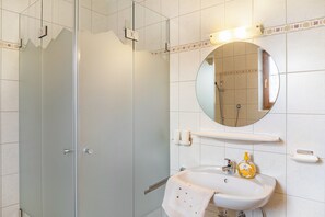 Ein Badezimmer mit einer Glaskabine zur Dusche, einem Waschbecken mit Handtuch und einem Spiegel darüber.