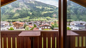 Blick von einem Balkon auf ein Bergdorf mit Häusern und bewaldetem Hang.