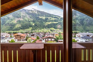 Une vue depuis un balcon donnant sur un village de montagne, avec ses maisons et une colline boisée.