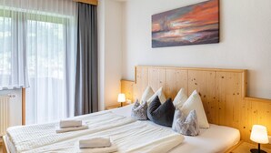 Ein Hotelzimmer mit einem großen Bett, einem Kopfteil, einem Bild an der Wand und einem Fenster mit Vorhängen.