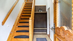 Eine hölzerne Treppe führt zu einem Raum mit einer dunklen Fußmatte und einer Tür mit aufwendigen Holzschnitzereien.