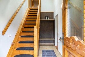 Un escalier en bois mène à une pièce dont le sol est recouvert d’un tapis sombre et qui possède une porte ornée de motifs complexes en bois sculpté.