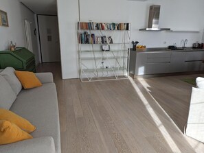 A modern living room with a grey sofa, a bookshelf, and a kitchen area with a sink and cabinets. - Apartment '5 Guests' with Balcony, Wi-Fi and Air Conditioning (Bergamo)