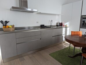 Eine moderne Küche mit einer Edelstahl-Dunstabzugshaube, einer integrierten Spüle und einem Essbereich mit rundem Tisch und einem grünen Teppich.