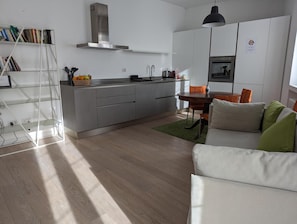 Moderni keittiö, jossa on sisäänrakennettu uuni, ruokailutila pöydän ja tuolien kera sekä olohuone, jossa on sohva.
