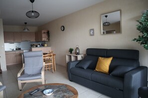 A living room with a sofa, armchair, coffee table, and a kitchen in the background. - Le Phare – 5-person apartment near Les Sables d'Olonne beach, Arago district (Les Sables-d'Olonne)