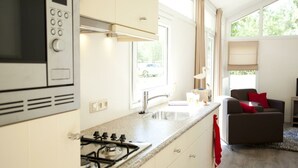 A modern kitchen with a stove, microwave, and sink, a dining area with a table and chairs, and large windows. - Holiday Home in Breskens With Terrace (Breskens)