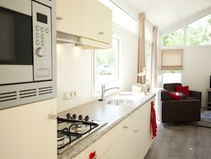 A modern kitchen with a stove, microwave, and sink, a dining area with a table and chairs, and large windows. - Holiday Home in Breskens With Terrace (Breskens)