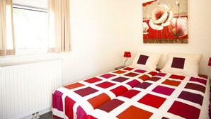 A bedroom with a bed, a window with curtains, a radiator, and a painting on the wall. - Holiday Home in Breskens With Terrace (Breskens)