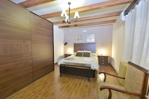 Un dormitorio con una cama de madera, mesitas de noche, una silla, techo de madera y un radiador.