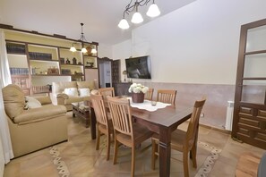 A living room with a sofa, dining table, chairs, and a TV mounted on the wall.