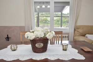Ein Esstisch mit einem Korbwicker-Korb, beschriftet mit 'HOME & FLOWER', gefüllt mit weißen Blumen, einer Spitzen Tischläufer und einem Kerzenhalter.