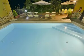 Une piscine avec des marches permettant d’y accéder, entourée d’un espace de détente extérieur et de parasols.