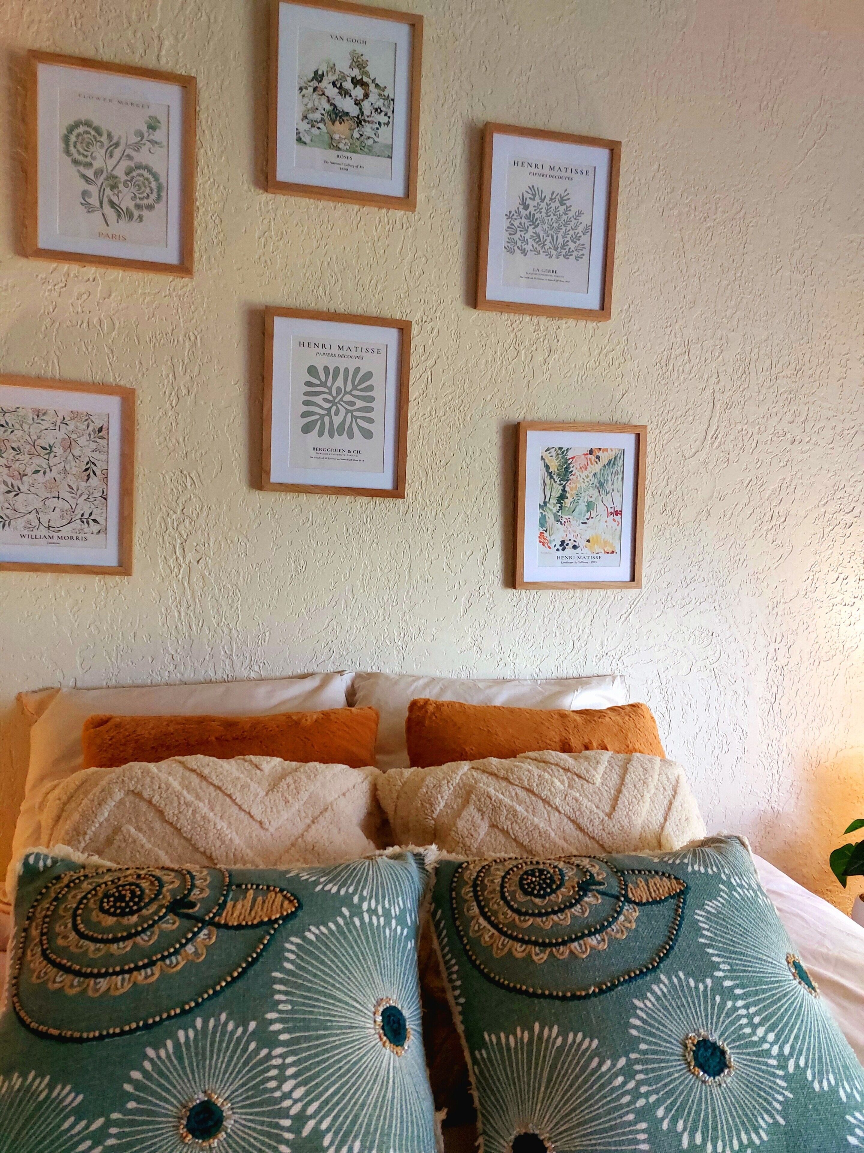 A bed with multiple pillows and a wall with framed botanical prints.