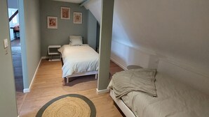 Une chambre à coucher avec un lit, une table de chevet, un canapé et une petite table. On y trouve des luminaires au plafond et une porte qui donne sur une autre pièce.