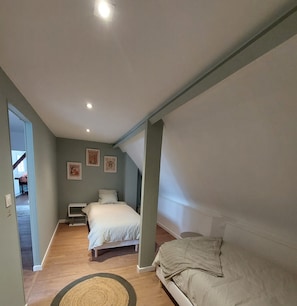 Ein Schlafzimmer mit Bett, Nachttisch, Sofa und kleinem Tisch. Es gibt Deckenleuchten und eine Tür zu einem anderen Raum.