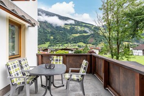 Ein Balkon mit Tisch und Stühlen mit Blick auf eine gebirgige Landschaft und Häuser.