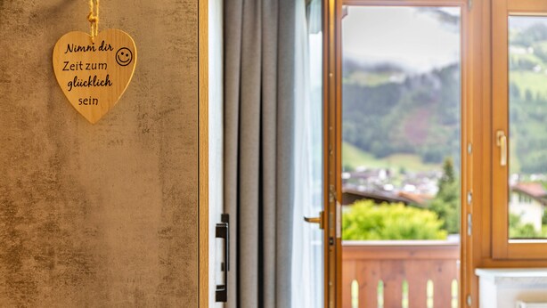 A wooden heart-shaped sign with text, a door, and a view of a landscape through a window. - Apartment Viktoria – Mountain Views, Terrace and Accessible Comfort (Ried im Zillertal)