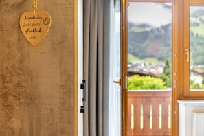 Ein herzförmiges Holzschild mit Schriftzug, eine Tür und ein Landschaftsblick durch ein Fenster.