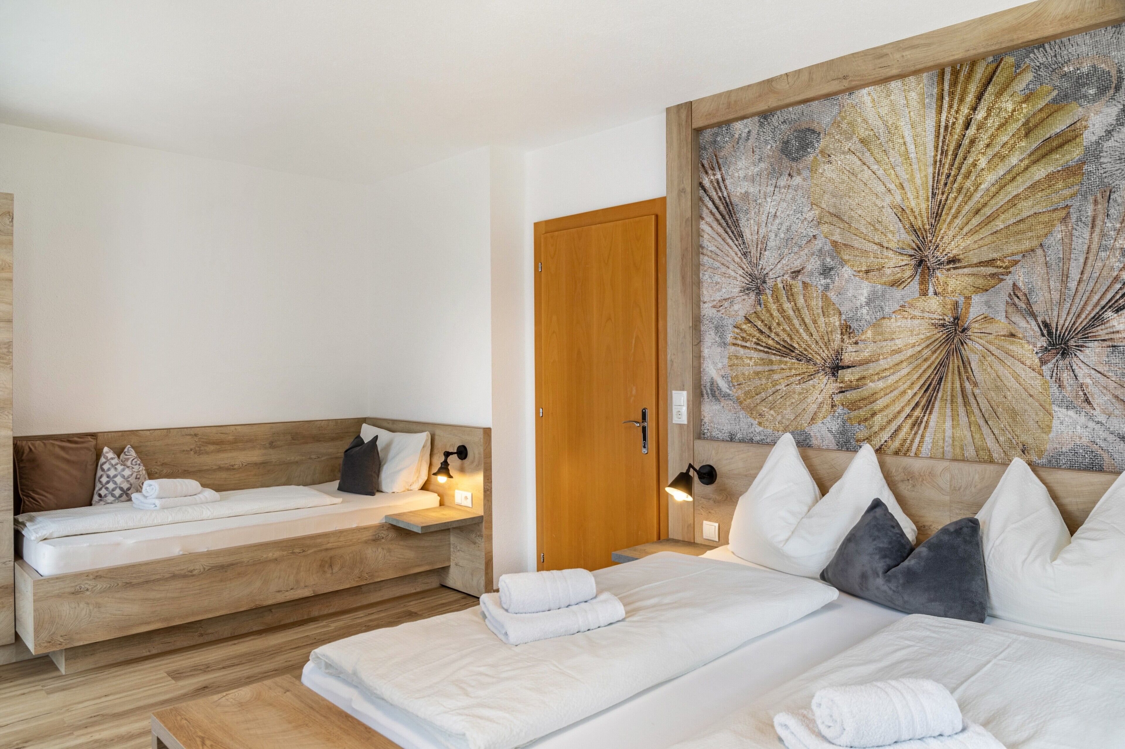 A modern bedroom with a large bed, a smaller sofa bed, and a wall-mounted artwork.